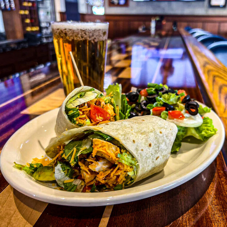 Chicken wrap with salad and beer on a bar table.