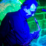 Musician playing saxophone on stage with microphone.