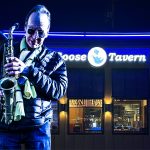Saxophonist performs outside Goose Tavern at night.