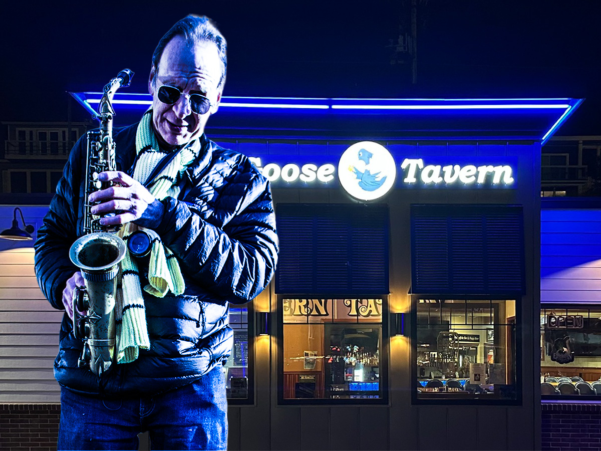 Saxophonist performs outside Goose Tavern at night.